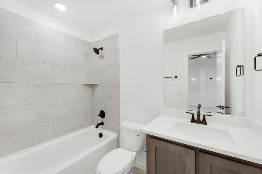 Bathroom with tiled tub surround, white quartz vanity, dark wood cabinets, and oil-rubbed bronze fixtures Bathroom with tiled tub surround, white quartz vanity, dark wood cabinets, and oil-rubbed bronze fixtures
