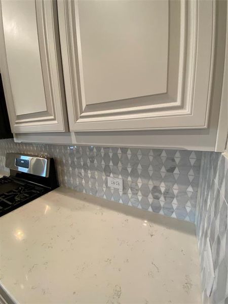 Close up of Monet quartz counters, decorative tile backsplash, and white cabinets.