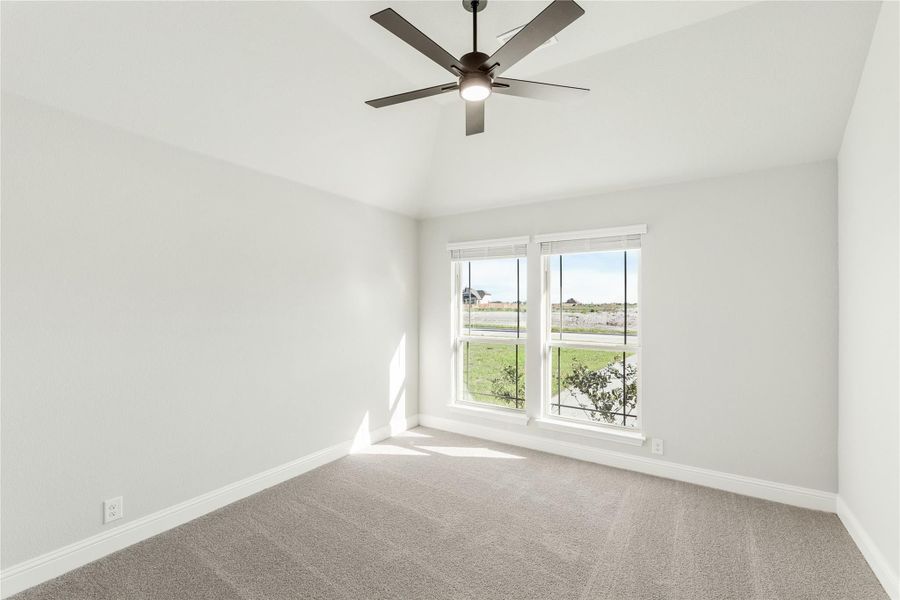 Empty bedroom with gray carpet, ceiling fan, and two windows overlooking a yard Empty bedroom with gray carpet, ceiling fan, and two windows overlooking a yard