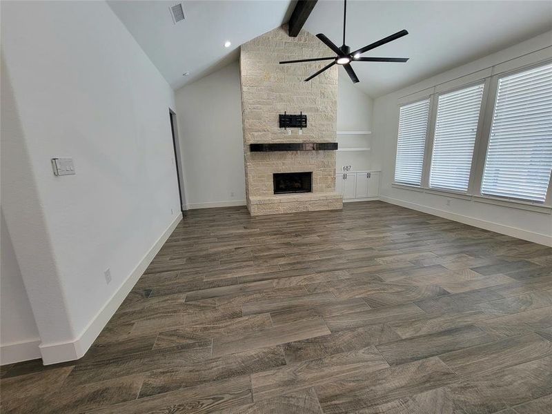 Unfurnished living room featuring a fireplace, dark hardwood / wood-style flooring, vaulted ceiling with beams, and ceiling fan