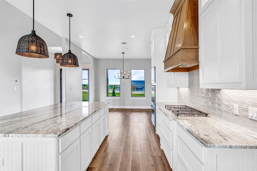 Kitchen with light wood-type flooring, light stone counters, custom range hood, pendant lighting, and white cabinets