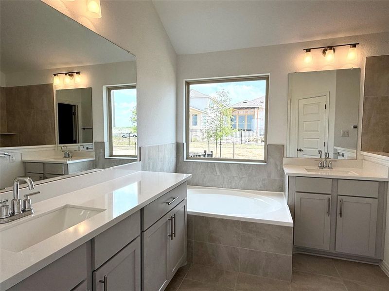 Bathroom featuring two vanities, a bath, plenty of natural light, and vaulted ceiling Bathroom featuring two vanities, a bath, plenty of natural light, and vaulted ceiling