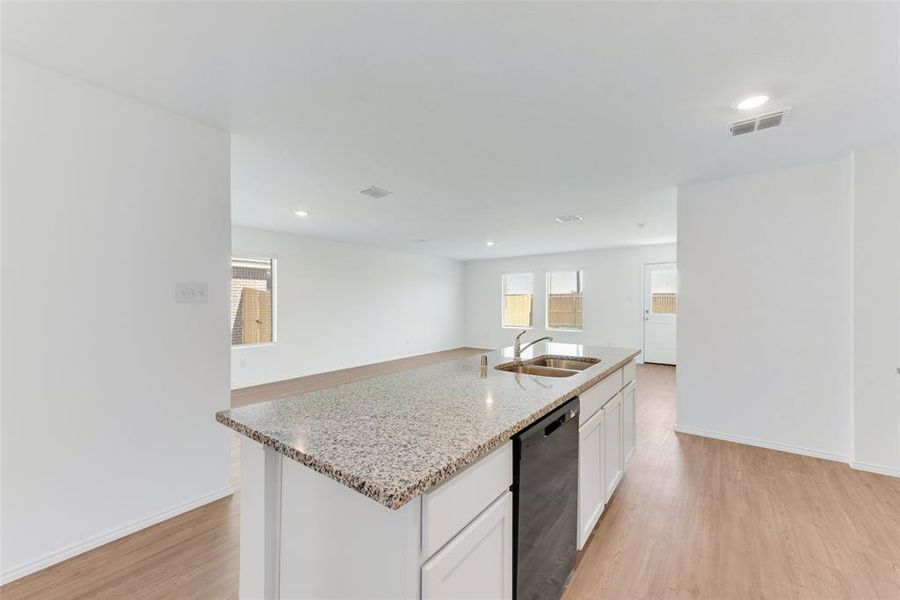 Kitchen featuring black dishwasher, light hardwood / wood-style floors, sink, an island with sink, and white cabinets