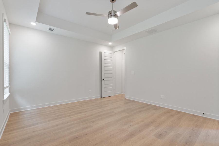 Tray ceiling with recessed lighting, wood-finish flooring, ceiling fan, and white paneled door Tray ceiling with recessed lighting, wood-finish flooring, ceiling fan, and white paneled door