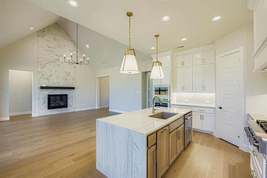 Kitchen featuring white cabinetry, high vaulted ceiling, a kitchen island with sink, decorative backsplash, and light wood-style floors