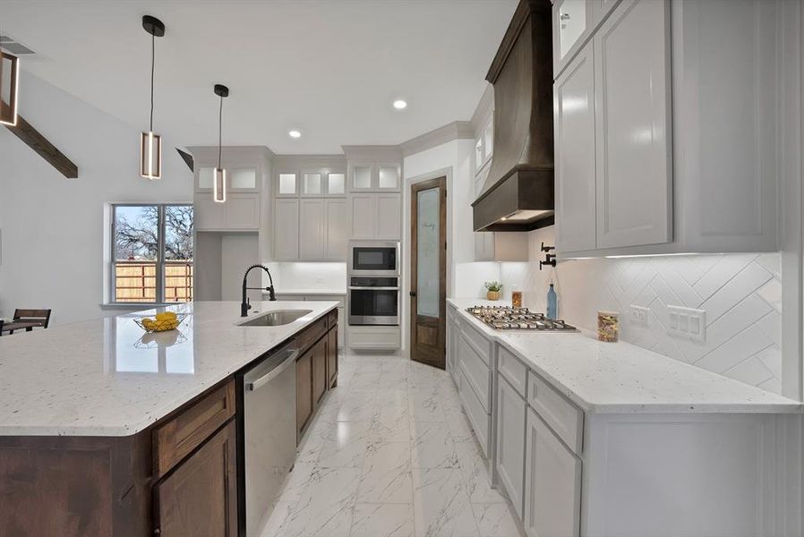 Kitchen featuring light stone countertops, light marble finish flooring, glass insert cabinets, hanging light fixtures, and appliances with stainless steel finishes