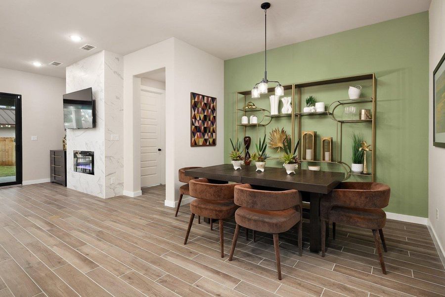 Elegant dining space features wood-look tile flooring and a sleek fireplace with a mounted television.
