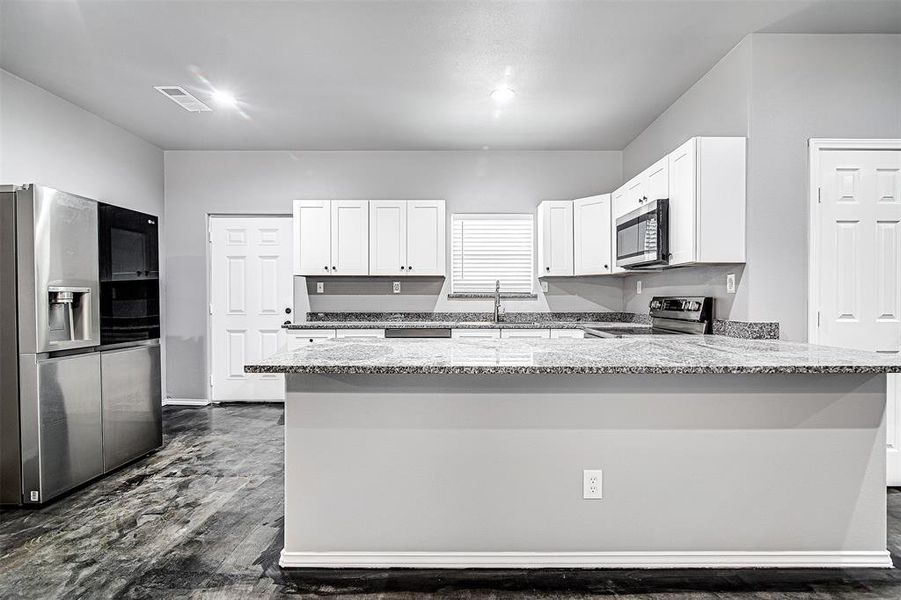 Kitchen featuring dark hardwood / wood-style flooring, light stone countertops, white cabinetry, stainless steel appliances, and kitchen peninsula