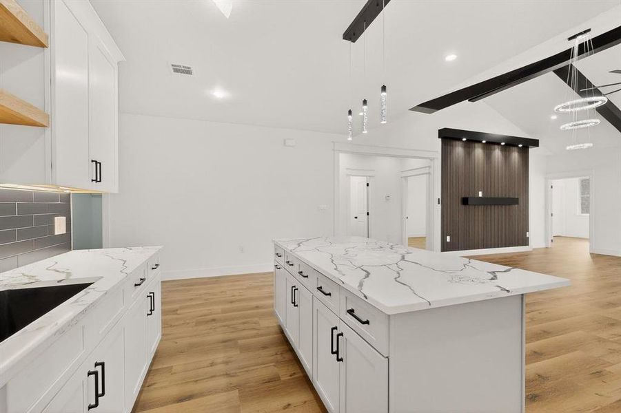 Kitchen featuring light stone counters, white cabinetry, a center island, light wood finished floors, and vaulted ceiling with beams Kitchen featuring light stone counters, white cabinetry, a center island, light wood finished floors, and vaulted ceiling with beams
