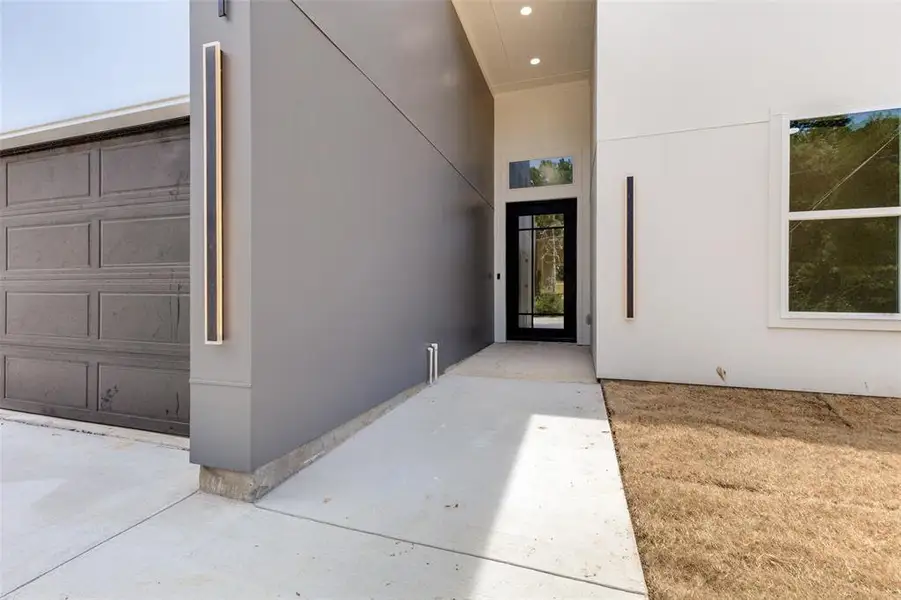 Contemporary exterior featuring a panel-paneled garage door, a recessed entry with a glass-paned door, and vertical outdoor lighting fixtures Contemporary exterior featuring a panel-paneled garage door, a recessed entry with a glass-paned door, and vertical outdoor lighting fixtures