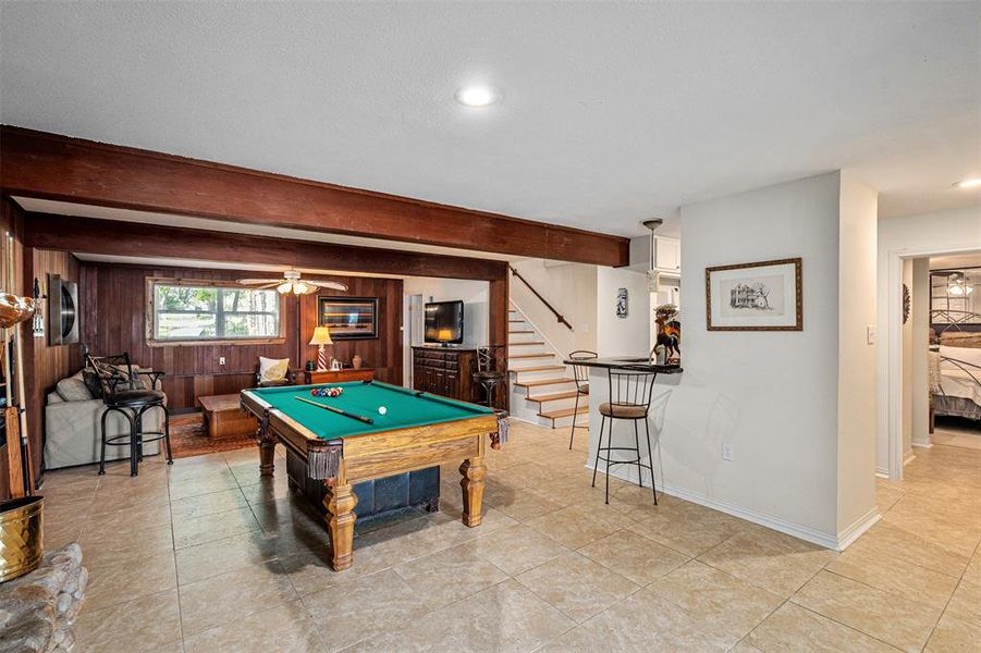 Spacious recreation room featuring tile flooring, exposed wood beams, and wood paneling