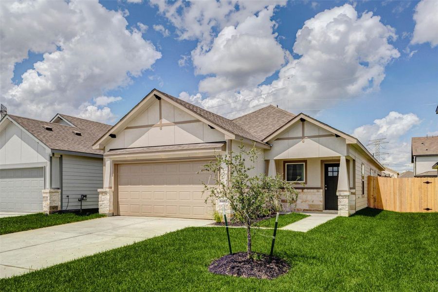 Angled exterior view featuring the front yard, young landscape tree, stone-accented façade, covered porch, and private side gate. The home offers a clean, modern traditional style with fresh sod, a wide concrete driveway, and a welcoming approach to the front entry.