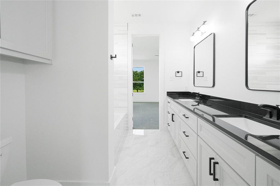 Bathroom with double vanity, a bathtub, and light marble finish floors