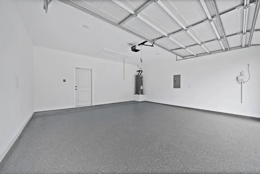 Spacious garage featuring a durable epoxy-coated concrete floor, white walls, and a paneled garage door Spacious garage featuring a durable epoxy-coated concrete floor, white walls, and a paneled garage door