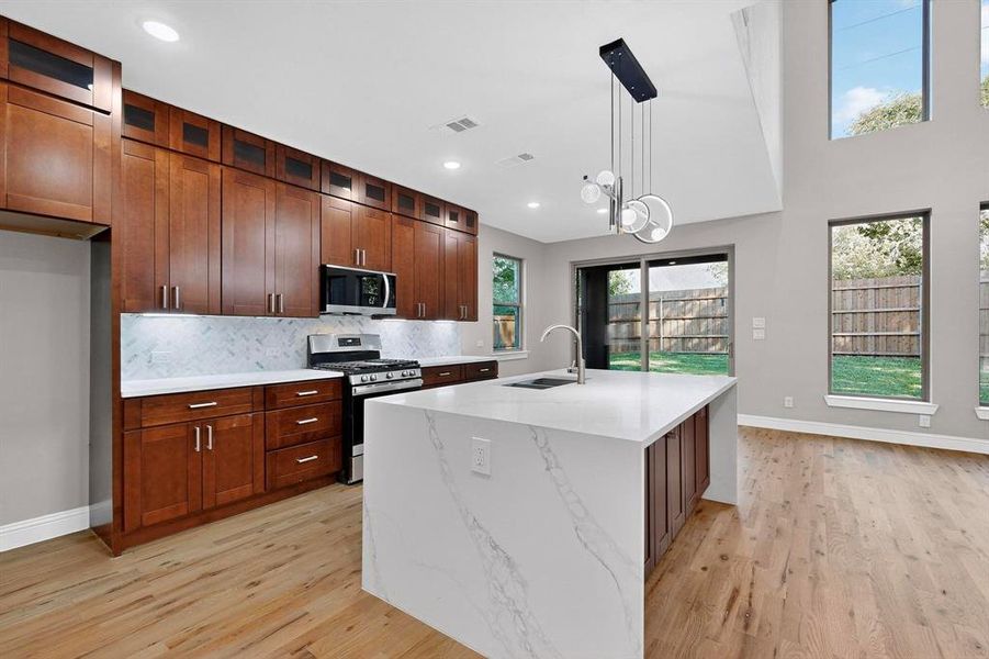 Kitchen with hanging light fixtures, appliances with stainless steel finishes, decorative backsplash, glass insert cabinets, and light stone counters