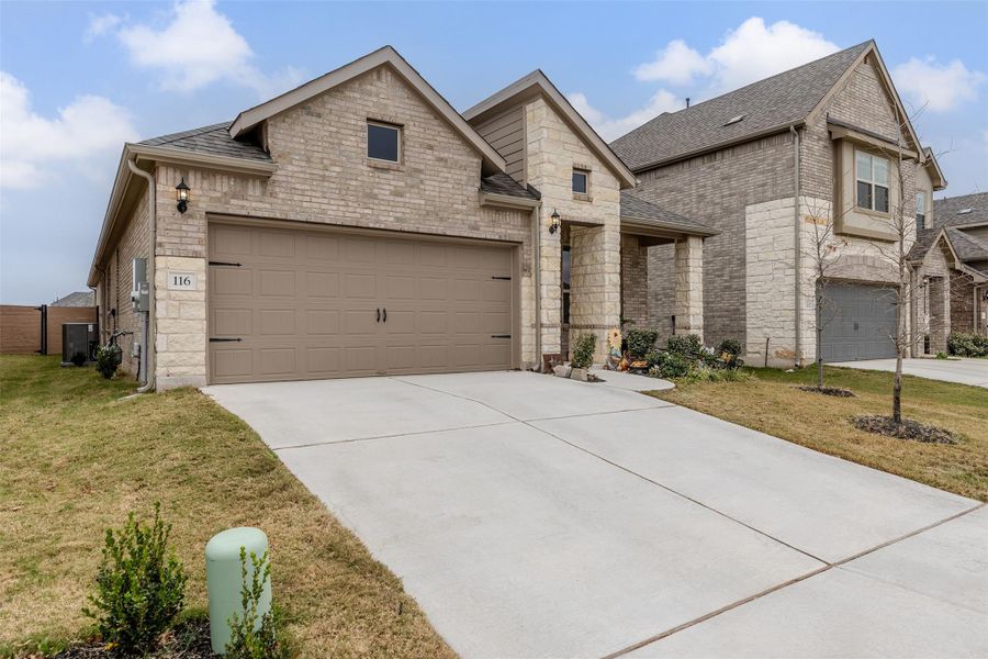 French country home featuring brick siding, a front lawn, a garage, and stone siding