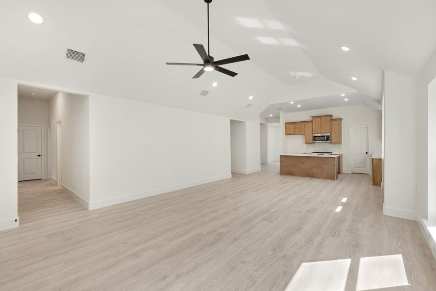 Open living area with vaulted ceiling, ceiling fan, and light wood floors flowing into kitchen with island