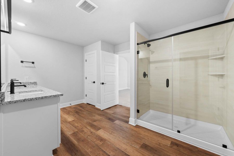 Bathroom featuring double vanity, dark wood finished floors, and a shower stall