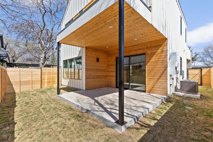 Rear view of property with board and batten siding, central AC unit, a lawn, a fenced backyard, and a patio