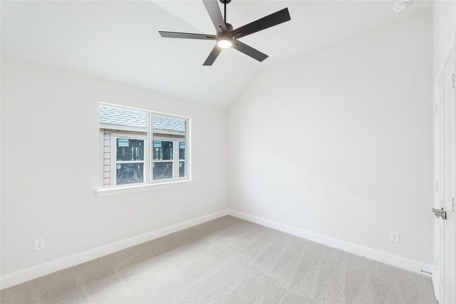 Empty bedroom with vaulted ceiling, black ceiling fan, carpet flooring, and a triple window