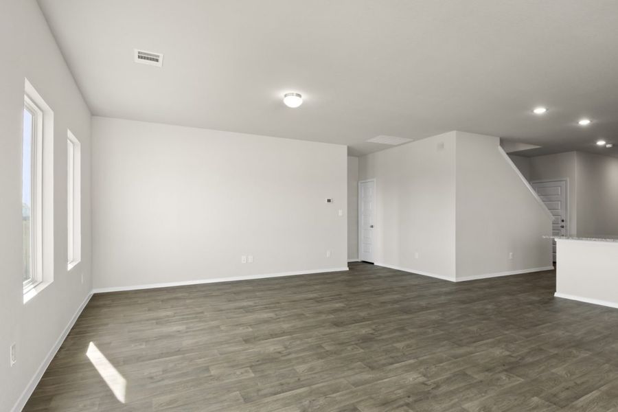 Image of a living room with grey walls, light brown vinyl flooring and a staircase in the distance