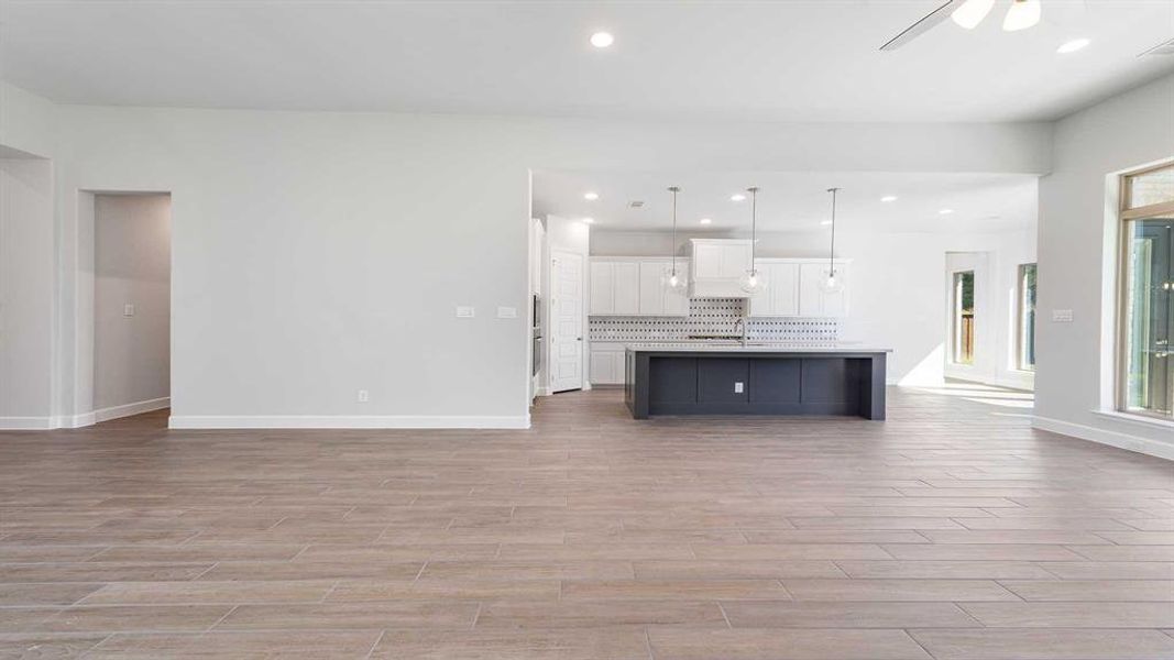 Kitchen with white cabinets, tasteful backsplash, an island with sink, pendant lighting, and light hardwood / wood-style floors