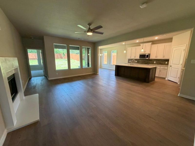 Open-concept living area featuring wood-finish flooring, a modern fireplace, and large windows providing abundant illumination