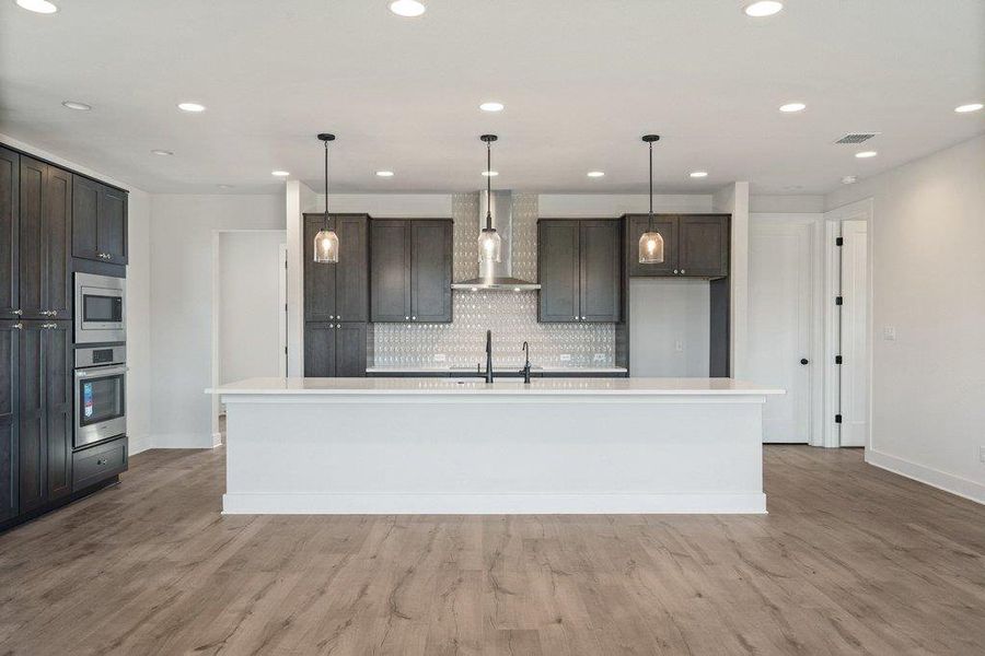 Kitchen featuring wall chimney exhaust hood, decorative backsplash, decorative light fixtures, a spacious island, and recessed lighting