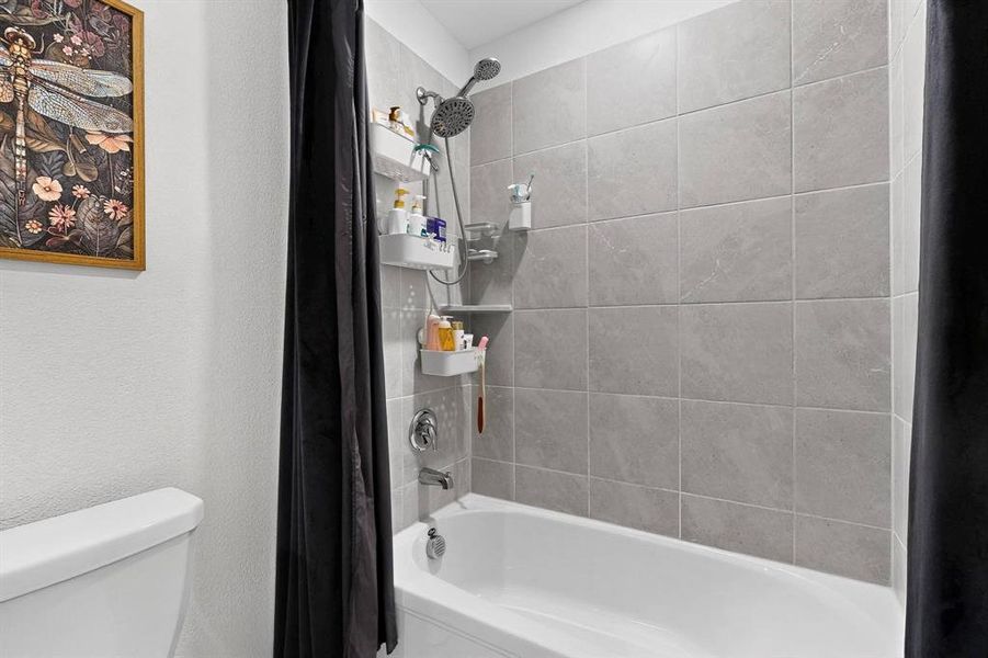 Full bath featuring shower / tub combo with curtain and a textured wall Full bath featuring shower / tub combo with curtain and a textured wall