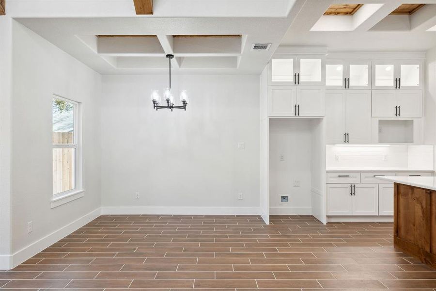 Unfurnished dining area featuring coffered ceiling, a notable chandelier, and beam ceiling