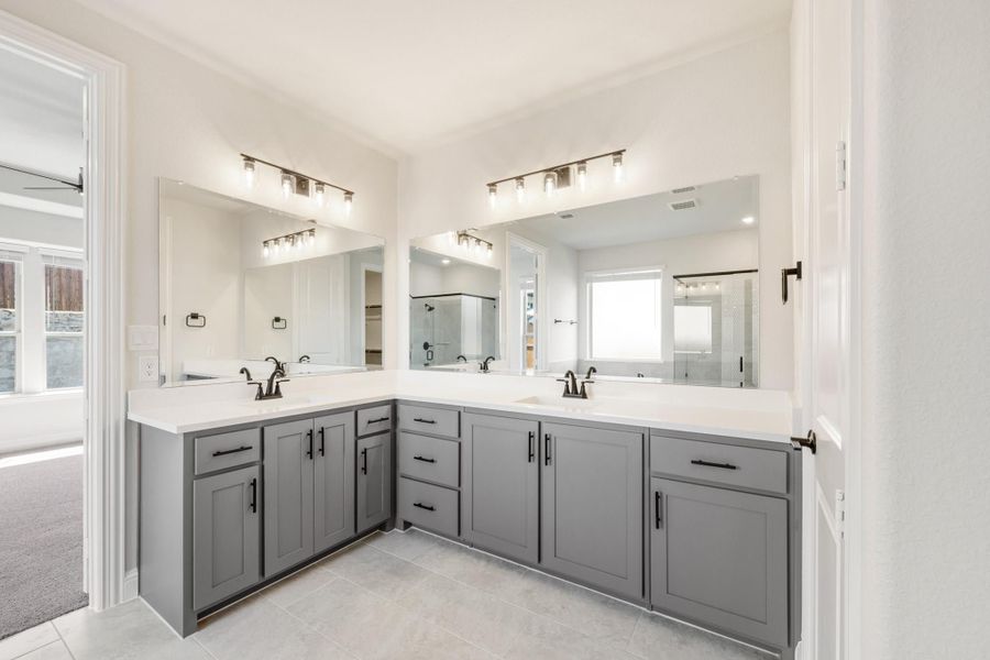 Bathroom with dual sinks, gray L-shaped vanity, white countertops, and large mirrors with overhead lighting