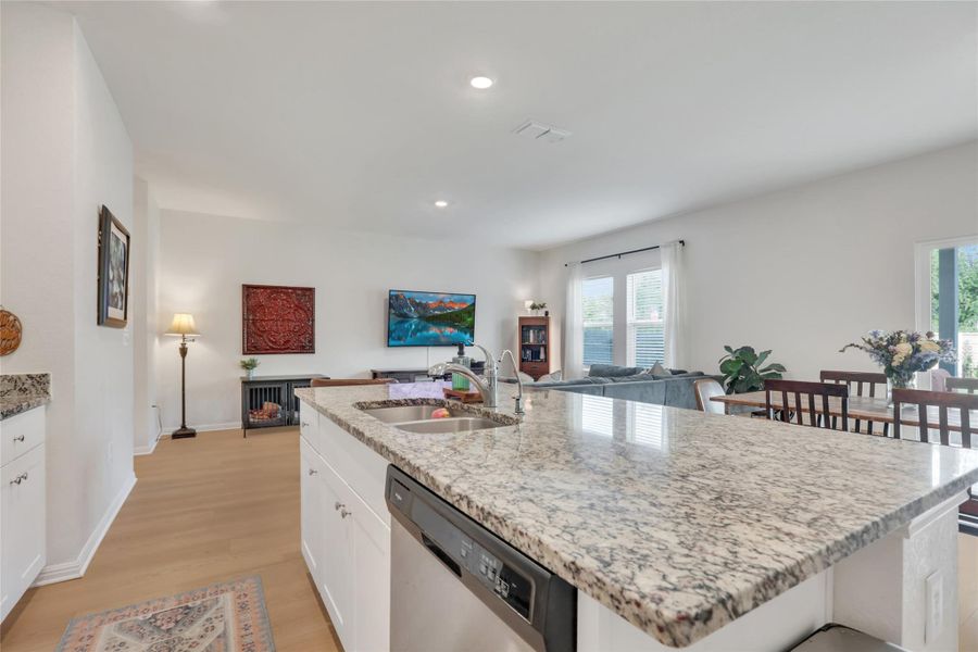 Kitchen featuring white cabinetry, stainless steel dishwasher, light stone countertops, open floor plan, and light wood finished floors