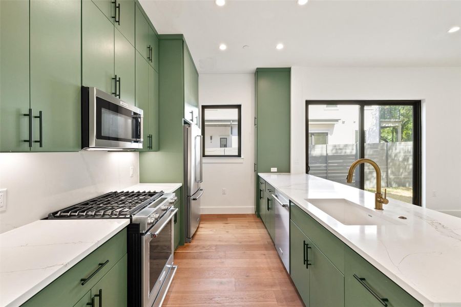 Kitchen with green cabinets, stainless steel appliances, light wood-type flooring, recessed lighting, and light stone countertops