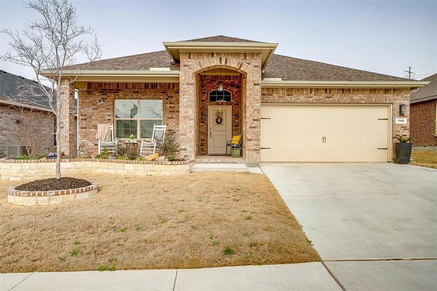 View of front of home with a shingled roof, concrete driveway, an attached garage, covered porch, and brick siding