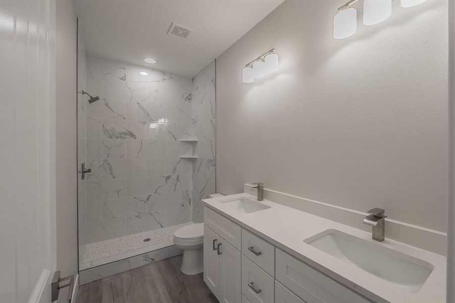 Bathroom with double vanity, a marble finish shower, and light wood-style flooring