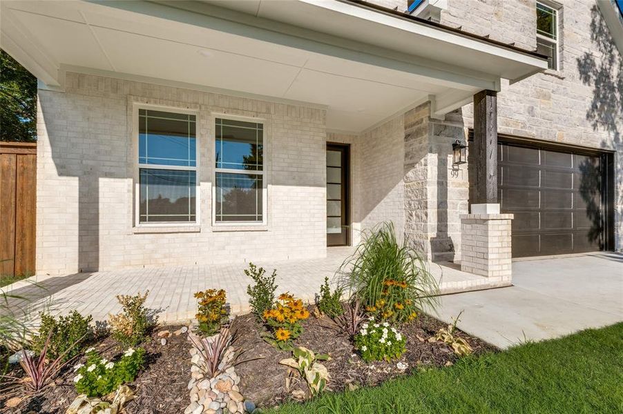 View of exterior entry with a garage, brick siding, a porch, and concrete driveway