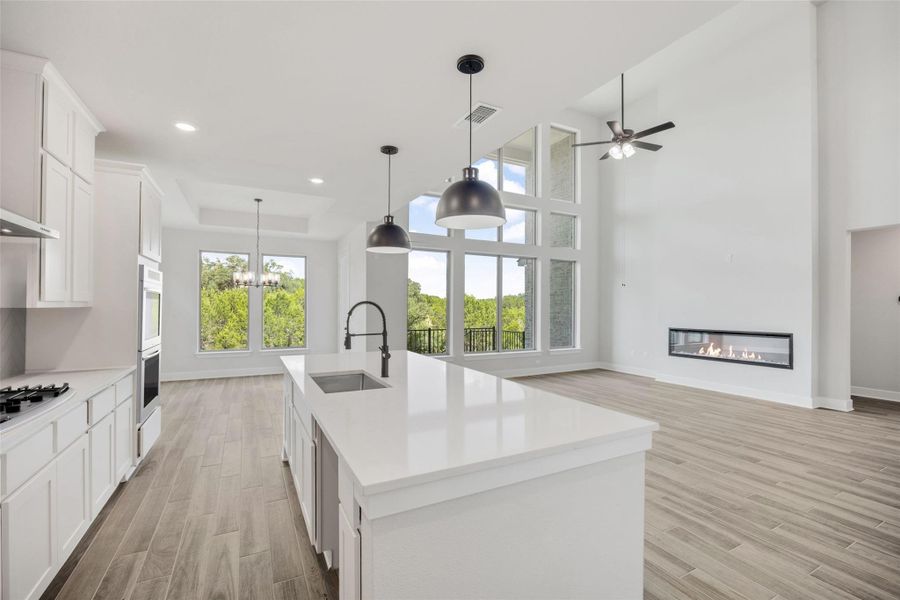 Kitchen featuring white cabinetry, decorative light fixtures, light wood-type flooring, a tray ceiling, and a center island with sink Kitchen featuring white cabinetry, decorative light fixtures, light wood-type flooring, a tray ceiling, and a center island with sink