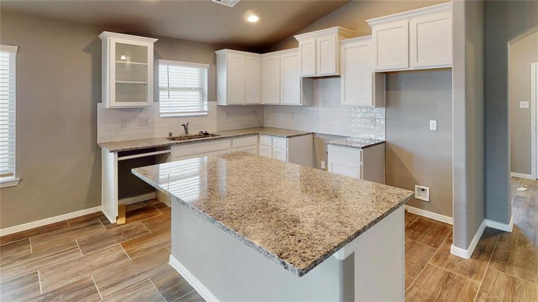 The spacious kitchen island offers ample countertop space for meal preparation and casual dining. The granite countertops and modern cabinetry with glass inserts enhance the kitchen's functionality and style. The open layout seamlessly connects the kitchen to the living area, making it an ideal spot for entertaining. This is a picture of an Elise Floor Plan with another Saratoga Homes.