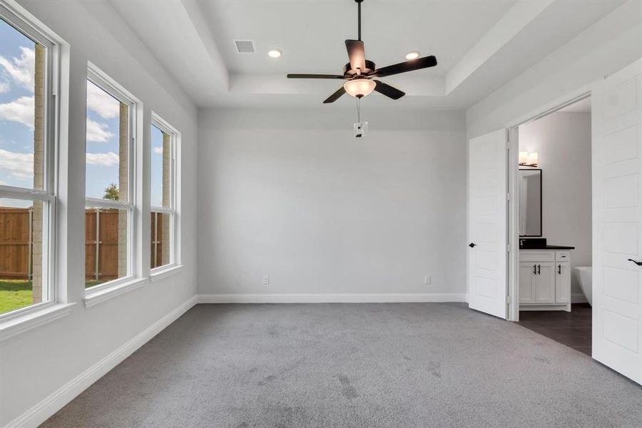 Carpeted spare room featuring ceiling fan and a raised ceiling