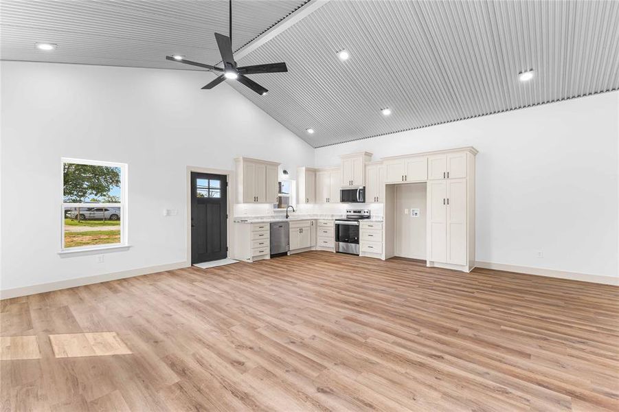 Kitchen featuring high vaulted ceiling, light countertops, light wood finished floors, stainless steel appliances, and open floor plan Kitchen featuring high vaulted ceiling, light countertops, light wood finished floors, stainless steel appliances, and open floor plan