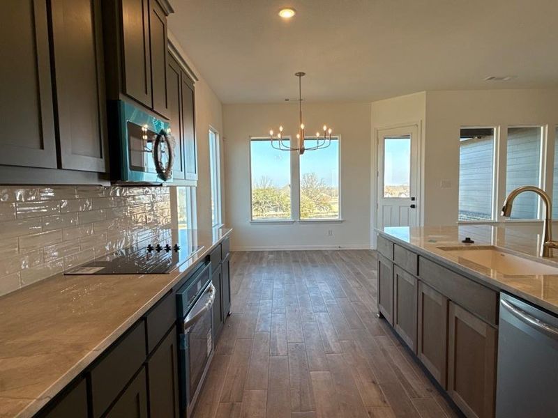 Kitchen with dark wood-style flooring, stainless steel appliances, hanging light fixtures, a chandelier, and light stone counters