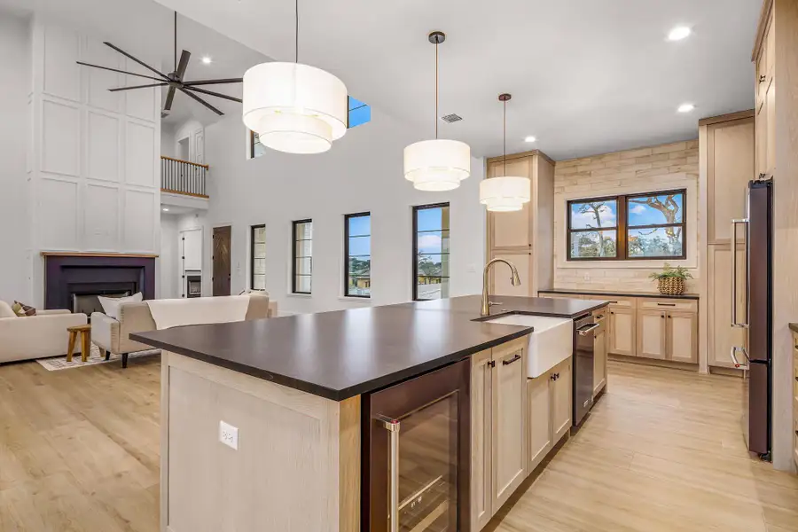 Kitchen with beverage cooler, dark countertops, open floor plan, decorative light fixtures, and a sink