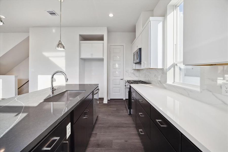 The clean lines of the cabinetry, paired with high-end stainless steel appliances and a pristine marble-patterned backsplash, create a luxurious yet practical kitchen environment. With plenty of counter space and storage, this kitchen is designed for both functionality and elegance.