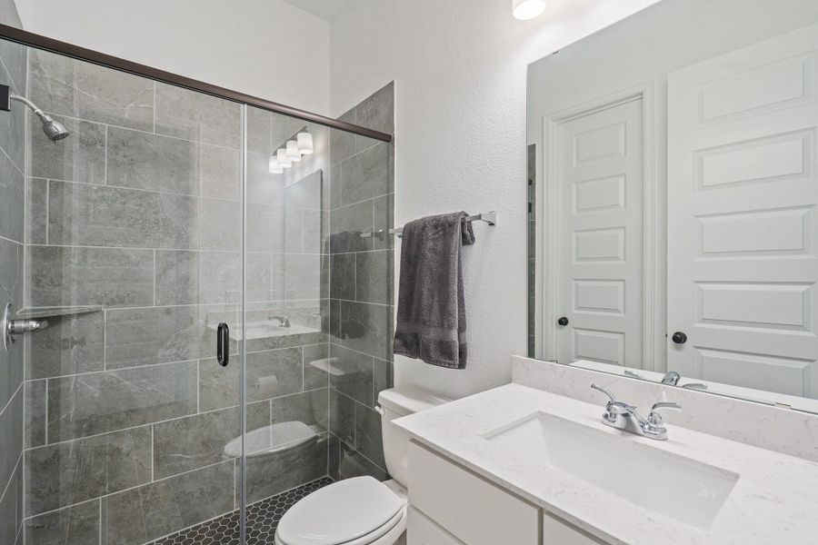 This modern bathroom features a sleek glass-enclosed shower with gray tiles, a clean white vanity with a marble countertop, offering a stylish and functional space.