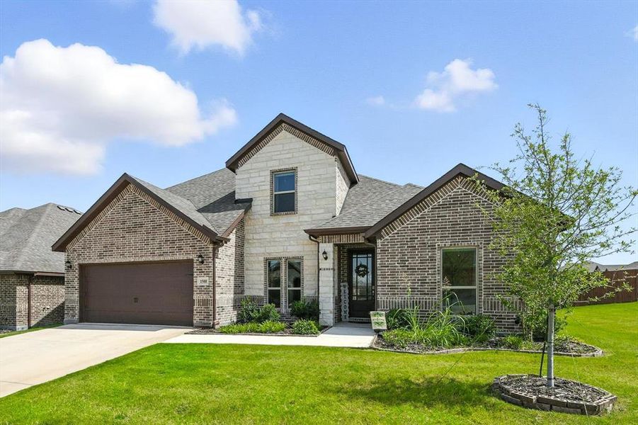 French provincial home featuring stone siding, a garage, a front yard, driveway, and a shingled roof