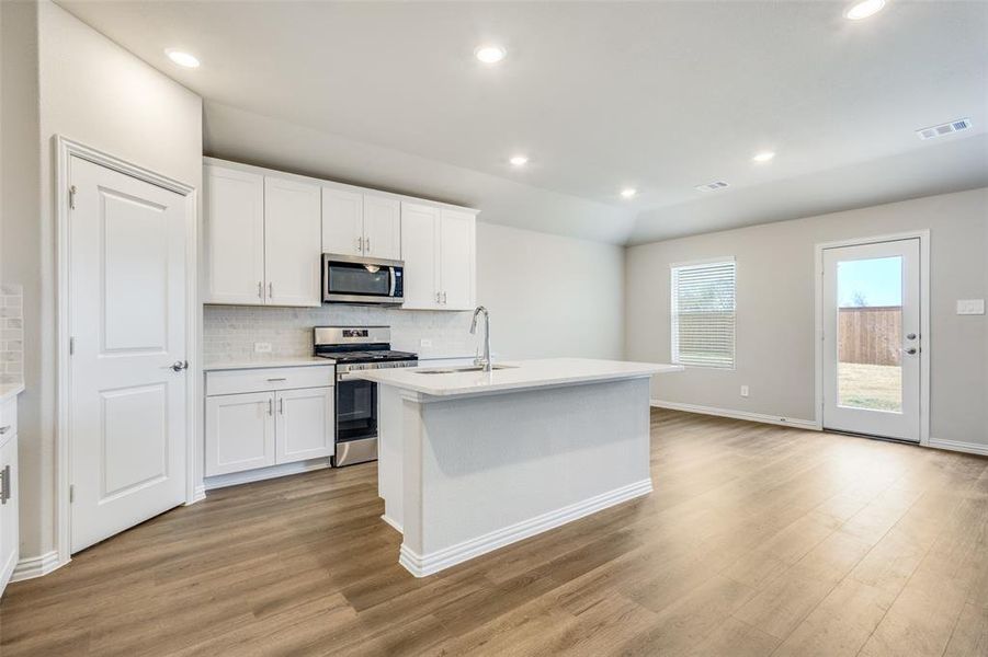 Kitchen featuring stainless steel appliances, a center island with sink, white cabinets, recessed lighting, and backsplash