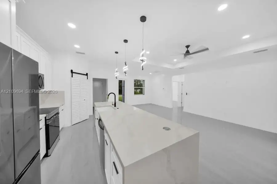 Kitchen featuring an expansive waterfall-edge island, white shaker-style cabinetry, recessed ceiling lighting, decorative pendant fixtures, and a black sliding barn door