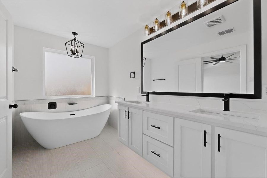 Bathroom featuring a wainscoted wall, double vanity, a freestanding tub, and tile walls
