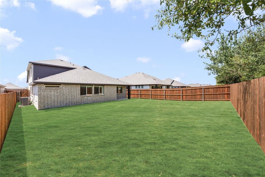 Large backyard with green lawn, wood privacy fence, and brick home exterior