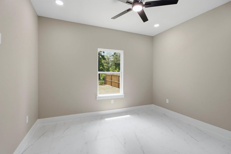 Spacious guest bedroom or home office with elegant marble-veined tiling, recessed LED lighting, a modern ceiling fan, and peaceful views of the backyard. Spacious guest bedroom or home office with elegant marble-veined tiling, recessed LED lighting, a modern ceiling fan, and peaceful views of the backyard.